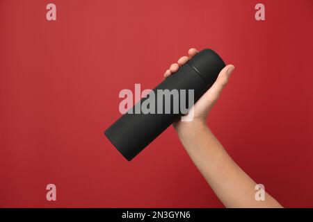 Woman holding modern black thermos on red background, closeup Stock Photo
