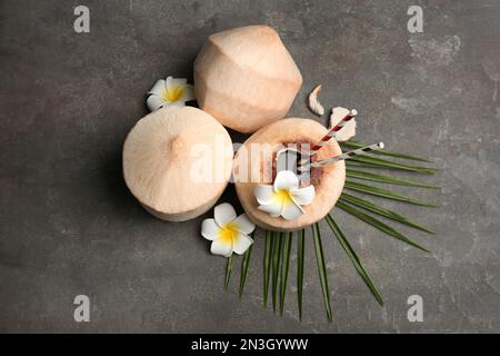 Young peeled coconuts with straw, palm leaf and beautiful flowers on grey table, flat lay Stock Photo