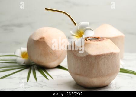 Young peeled coconut with straw and flowers on white marble table. Space for text Stock Photo