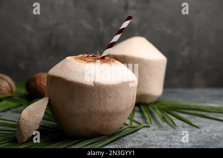 Young peeled coconut with straw and palm leaf on grey table Stock Photo