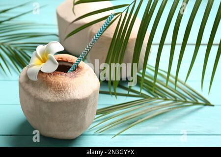 Young peeled coconuts with palm leaves and flower on light blue wooden table Stock Photo