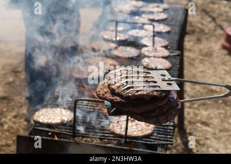 A hamburger cookout in Grand Island, Nebraska, USA, with numerous burgers on a long grill and prepared hamburger patties held in tongs in the foreg... Stock Photo