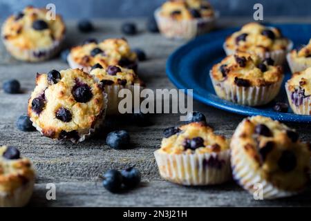 Several homemade blueberry muffins scattered around on a rustic wooden table. Stock Photo