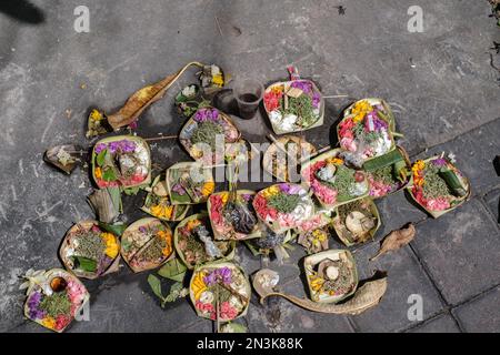 Colorful Canang sari offerings arranged in a flat lay on a paved road Stock Photo