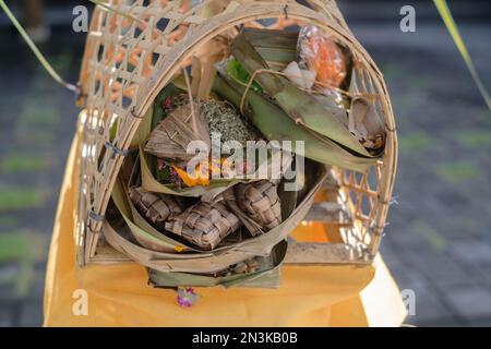 Sacred Canang sari offerings arranged on traditional bamboo-weaved spirit house symbolize balance and harmony in Balinese Hindu culture Stock Photo