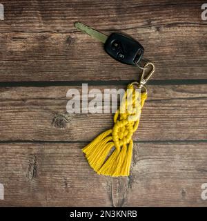 Top view of the handmade macrame key chain hanging on the car key isolated on the wood background. Stock Photo