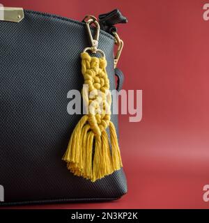 Close-up view of the handmade Macrame key chain hanging on the black hand bag isolated on the red background. Stock Photo