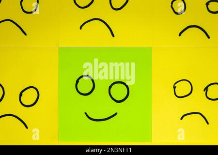 Unhappy and happy concept. Background of sticky notes. Green sticky note is among yellow sticky notes. Stock Photo