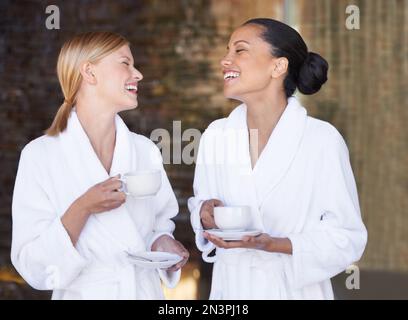 We should do this more often. Two female friends in bathrobes at the day spa enjoying some tea. Stock Photo