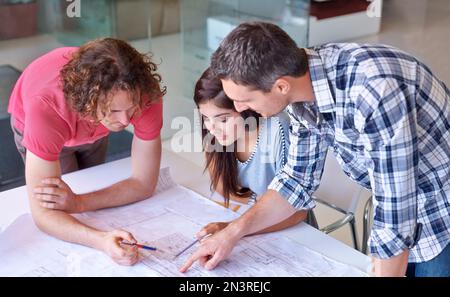 Working on their blueprints - Architecture. Three architects working on their blueprints together in the boardroom. Stock Photo