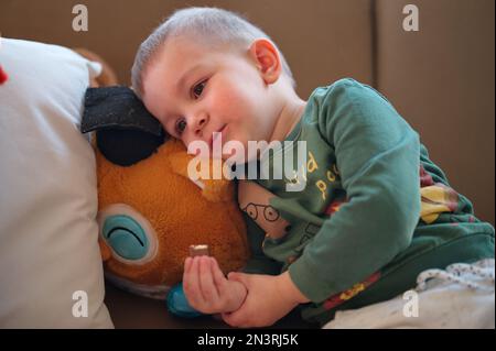 Portrait of cute little toddler sitting on a sofa and eating chocolate Stock Photo