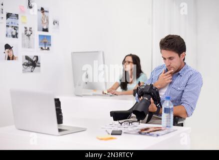 Using the tools of the trade. Two photographers sitting in their office working on layouts and inspecting their equipment. Stock Photo