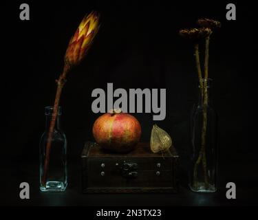 Still Life with Dried Flowers in Glass Bottles Next to Pomegranate and Physalis on Old Wooden Casket Stock Photo