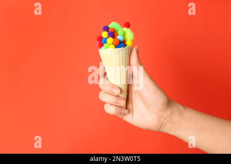 Woman holding ice cream waffle with fluffy balls on coral background, closeup Stock Photo