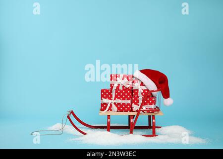 Stylish sleigh with Christmas gifts and Santa hat in pile of snow on light blue background, space for text Stock Photo
