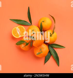 Fresh tangerines with green leaves on coral background, flat lay Stock Photo