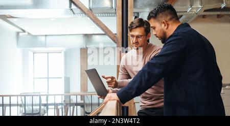 business man discussing a tech project with his colleague in an office. Two business men using a laptop on an interior balcony. Male professionals wor Stock Photo