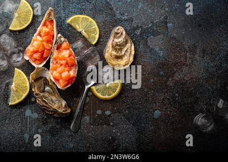 Delicious salmon tartare raw chopped in cubes served in oyster shells with lemon wedges and ice on blue stone rustic background, seafood appetizer or Stock Photo