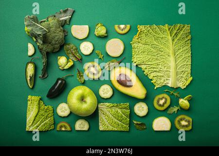Creative minimalistic healthy organic food concept made of green fruit and vegetables on green background flat lay: avocado, kale, broccoli, Brussels Stock Photo