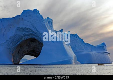 Large iceberg with hole, small boat in front of it, midnight, summer in the Arctic, Ilulissat, Disko Bay, North America, Greenland, Denmark Stock Photo