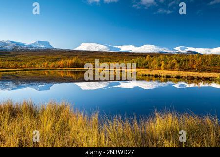 Mountain group Lapporten and snowy mountains of Abisko National Park reflected in small pond, autumnal fell landscape, Abisko, Lapland, Sweden Stock Photo