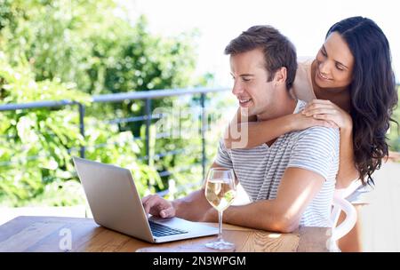 Surfing the web outside. A young couple sitting using their laptop on the patio. Stock Photo