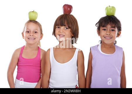Eating healthy from an early age. Group of three children balancing apples on their heads. Stock Photo