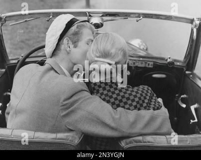 In the 1950s. A young couple is sitting in a convertible car. He has his arm around her and kisses her on the cheek. Sweden 1954 Stock Photo