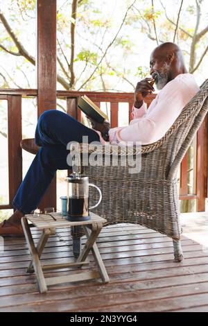Side view of bald african american senior man reading book while sitting on chair in balcony Stock Photo