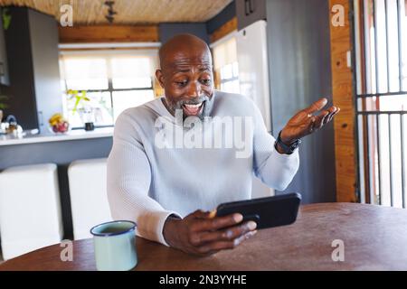 Happy bald african american senior man gesturing while video calling on cellphone in log cabin Stock Photo