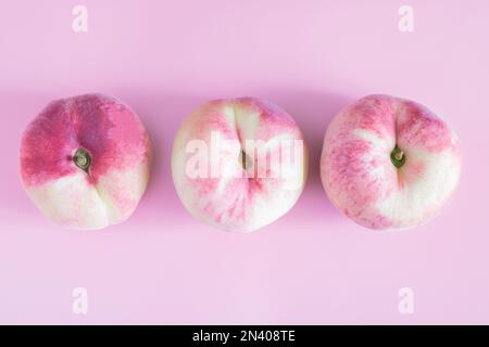 flat peaches isolated on pink background. three figs peach, located in the center. fresh delicious peaches. copy space Stock Photo