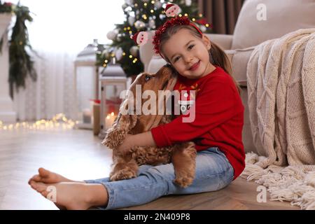 Cute little girl with English Cocker Spaniel in room decorated for Christmas Stock Photo