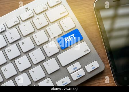 NFT or non fungible token concept with keyboard and blue button and a mobile phone on a desk. Stock Photo