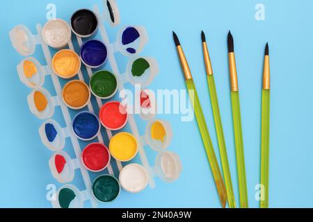 Colorful paints in jars on a blue background near the brushes. Color palette. Concept-creativity and school theme. Open cans of gouache paint are near Stock Photo