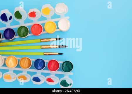 Colorful paints in jars on a blue background near the brushes. Color palette. Concept-creativity and school theme. Open cans of gouache paint are near Stock Photo