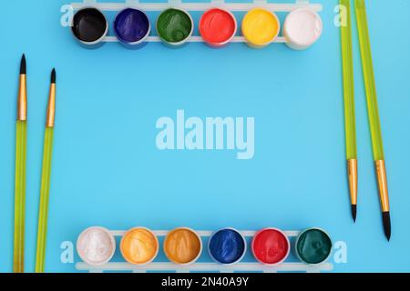 Colorful paints in jars on a blue background near the brushes. Color palette. Concept-creativity and school theme. Open cans of gouache paint are near Stock Photo