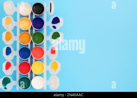 Multi-colored paint in cans on blue background. Palette of colors. Concept - creativity and school theme. Open jars of gouache paint, on a blue backgr Stock Photo
