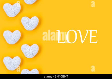 Many white knitted hearts with an inscription "love" on yellow background. Concept of Valentine day. Greeting card for Valentine,  Mother day or birth Stock Photo