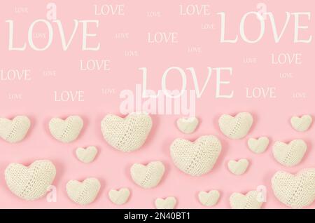 Many white knitted hearts with an inscription "love" on pink background. Concept of Valentine day. Greeting card for Valentine,  Mother day or birthda Stock Photo