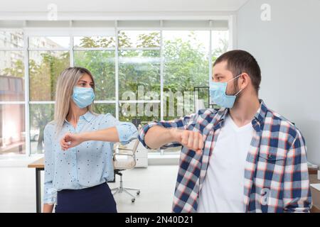 Office employees in masks greeting each other by bumping elbows at workplace Stock Photo
