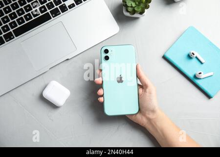 MYKOLAIV, UKRAINE - JULY 10, 2020: Woman holding Iphone 11 Green at table, top view Stock Photo