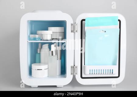 Open cosmetic refrigerator with skin care products on light background Stock Photo