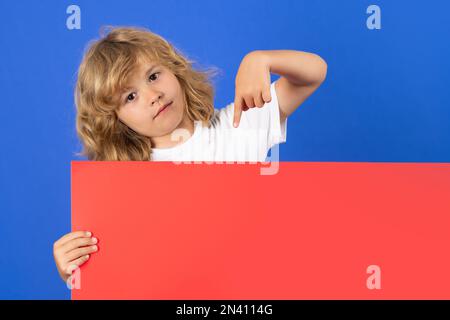 Kid boy points his finger down at empty space. Portrait of child isolated on studio background. Copy space. Stock Photo