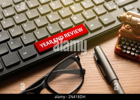 Glasses,pen, miniature typewriter and computer keyboard with red button written with Year End Review. Stock Photo