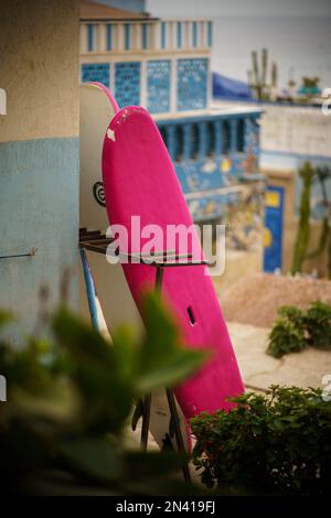 A vertical shot of colorful surfboards leaning on an old house wall Stock Photo