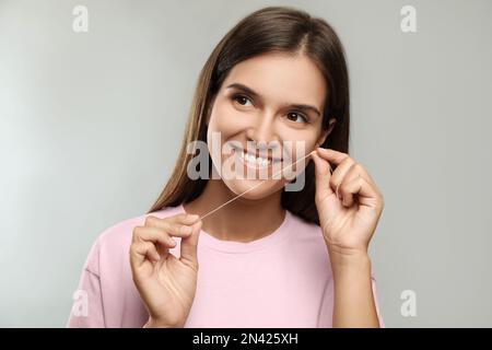 Young woman flossing her teeth on light grey background. Cosmetic dentistry Stock Photo