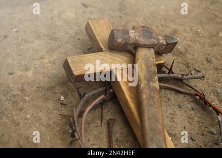 Crown of thorns, wooden cross and hammer on ground. Easter attributes Stock Photo