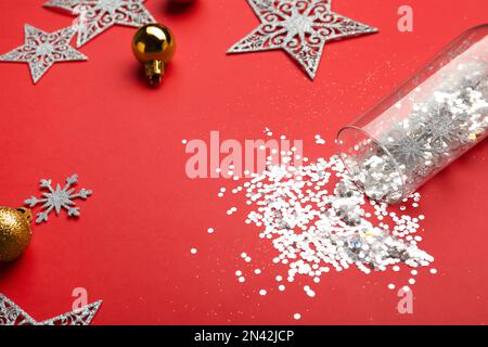 Composition with shiny confetti spilled out of champagne glass near Christmas decorations on red background, closeup Stock Photo