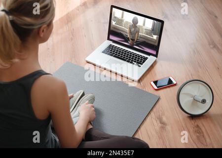 Yoga teacher conducting virtual class at home on a video conference. Young beautiful woman doing an online yoga class in her living room with laptop. Home fitness and workout concept Stock Photo