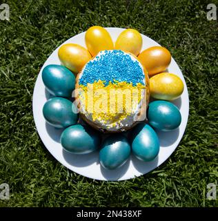 Composition with multi-colored blue and yellow Easter eggs around the Easter cake in the colors of the Ukrainian flag. Ukrainian traditions. Support U Stock Photo